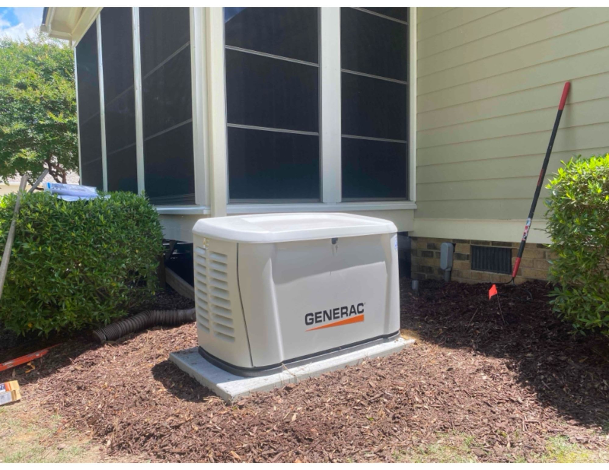 Generac standby generator installed in a landscaped bed beside a residential home